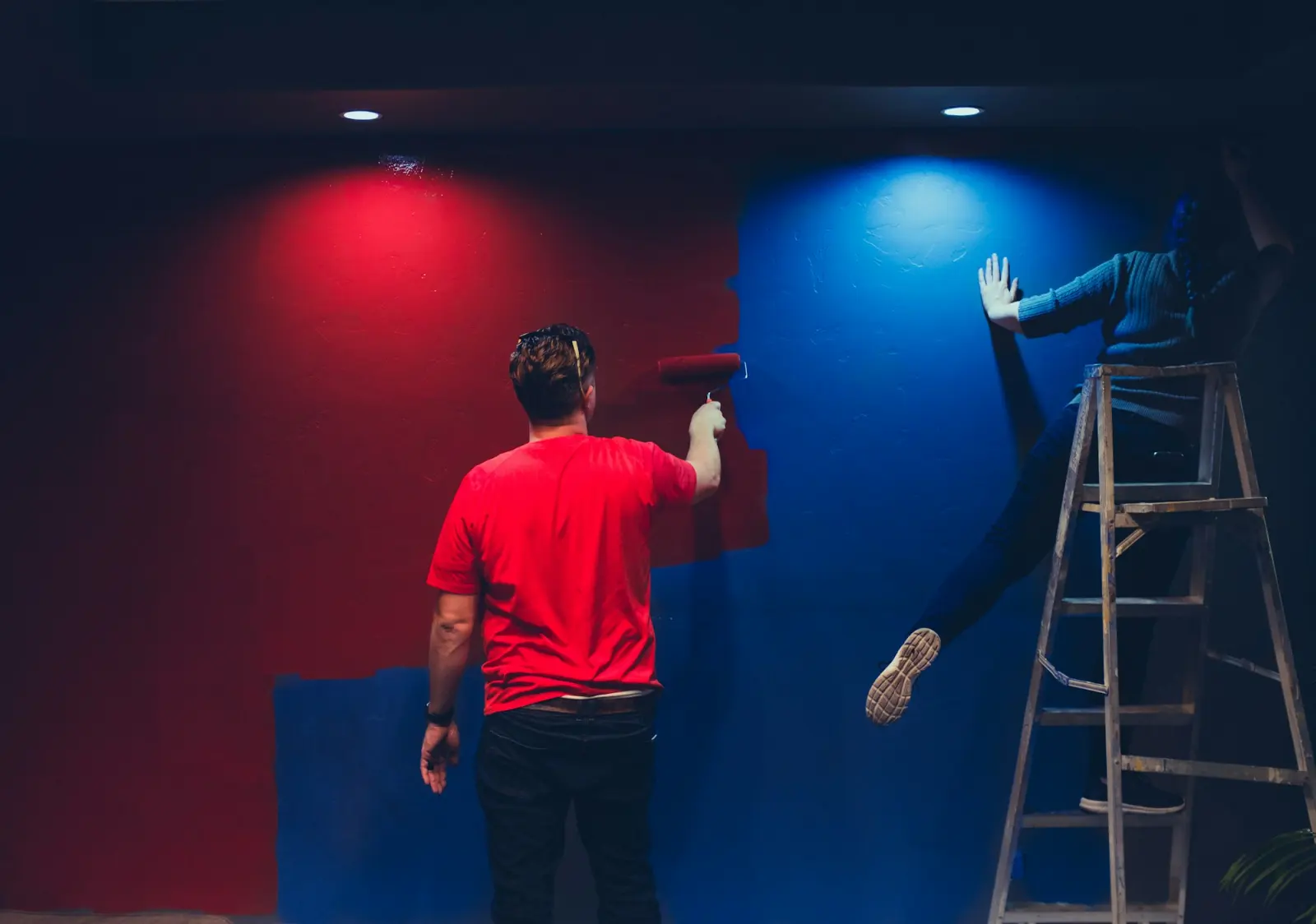Due persone che dipingono una parete metà rossa e metà blu